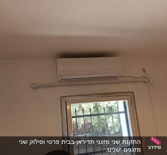 מזגן מותקן על קיר מעל חלון עם סורגים